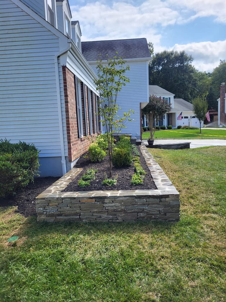 After — the stacked-stone planter wall and its new plantings running along the side of the house